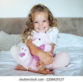 Children, teddy bear and girl child hug her stuffed animal with a smile in her house. Portrait of kid, happy and safe with an adorable or cute female holding a fluffy toy sitting on a bed