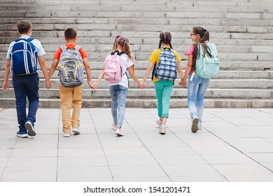 Children teenagers in colorful clothes with backpacks are walking up the stairs to school. Back view. - Shutterstock ID 1541201471