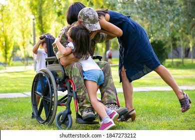 Children And Their Mom Hugging Disabled Retired Military Father In Park. Veteran Of War Or Returning Home Concept