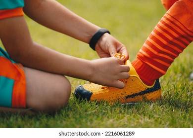 Children tie shoelaces at grass sports field. Little boy helping to friend with tying shoelaces in soccer cleats