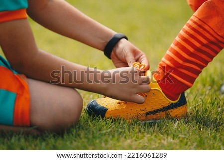 Children tie shoelaces at grass sports field. Little boy helping to friend with tying shoelaces in soccer cleats