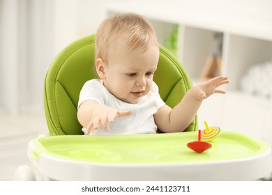 Children toys. Cute little boy playing with spinning tops in high chair at home