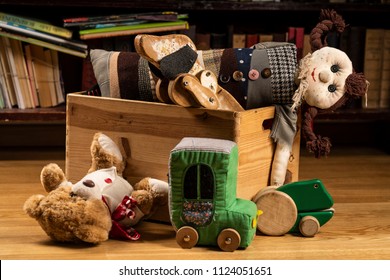 Children toys in a wooden box, books in the background on wooden floor. Teddy bear, wooden dog toy, rag doll, toy car, wooden green frog