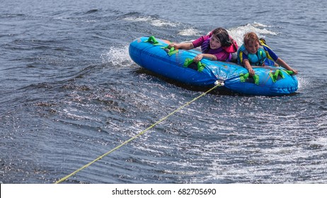 Children Tubing Behind Motorboat On Lake In Summer