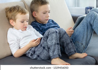 Children Using Tablet Computer. Brothers Sitting On Couch At The Living Room And Playing With Tablet Device. Education, Science, Technology, Children's Security, Internet Safety Concept