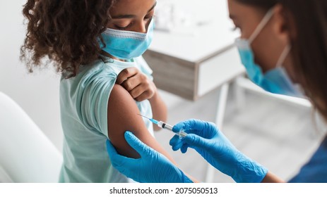 Children Vaccination. Preteen Black Girl Getting Vaccinated For Covid-19 Prevention Sitting In Clinic. Medical Worker Wearing Face Mask Injecting Kid Patient. Antiviral Immunization. Cropped