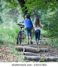 Children walking  in forest.  Llittle boy walking with his bike high up