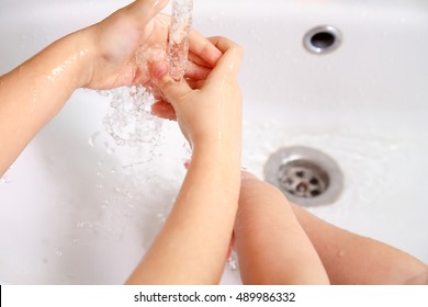 Children washing hands in a white sink under running water