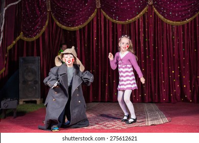 Children Wearing Clown Make Up and Costumes Having Fun and Performing on Stage with Red Curtain