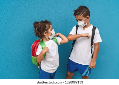 Children wearing face protective mask going back to school during corona virus pandemic - Little kids doing new social distance greeting bumping elbows - Healthcare and education concept