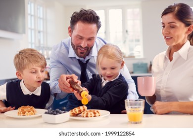 Children Wearing School Uniform In Kitchen Eating Breakfast Waffles As Parents Get Ready For Work