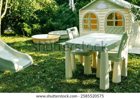 Children's backyard play area with a plastic slide, sandbox, table, chairs, and a small playhouse on the lawn. Perfect for outdoor fun, summer activities, and family entertainment.