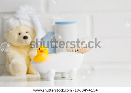 Children's bath accessories. Baby care. Bear with a towel on his head, a brush and bottles of shampoo. A miniature bubble bath and a yellow rubber duckling for bathing.