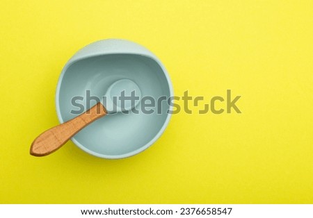 Children's blue plate with a spoon on a yellow background, close-up. Baby diet and calories for breakfast, lunch and dinner. Copy space for text, complementary. Daily calorie intake