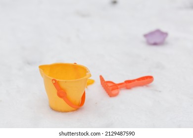 Children's Bucket And Rake Lie On White Snow, Background, Winter, Macro, Product Photography, Children's Toys.