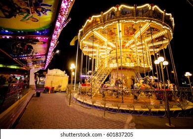 Children's Carousel At An Amusement Park In The Evening And Night Illumination. Amusement Park At Night. Amusement Park, Picture For The Background.