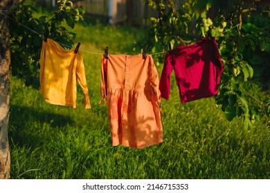Children's colored clothes dry on clothesline in the garden in nature under rays of the sun after laundering. Protection against fading of colored fabrics. Organic baby washing powders and detergents