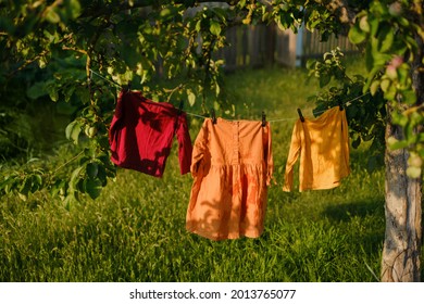 Children's colored clothes hang on a clothesline and dry after washing in nature under a tree in the garden. Clothes flutter in the wind. Hypoallergenic washing powder for babys clothes. 