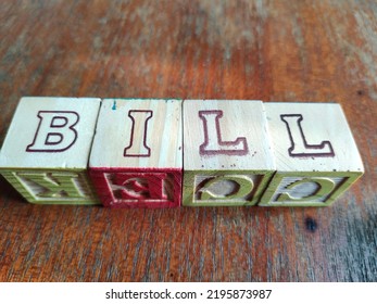 Children's Colourful Wooden Alphabet Building Block Letters That Spell Out The Word BILL On A Wooden Background. Business And Text Concept. Negative Space