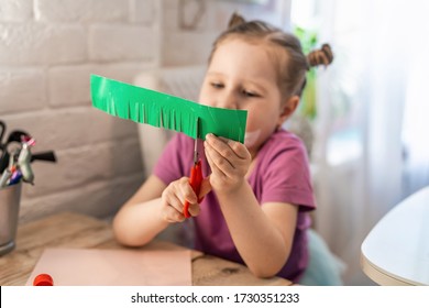 Children's Creativity. A Little Girl Enthusiastically Cuts Colored Cardboard With Scissors, Cutting Small Strips In The Form Of Grass On It. Skill To Cut With Scissors, Learning New Things.