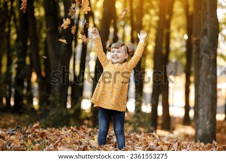 Childrens day. Happy adorable child girl 3-4 years having fun, playing with fallen leves, smiling, enjoying nice and sunny autumn day outdoors. Happy Childhood dream and freedom concept