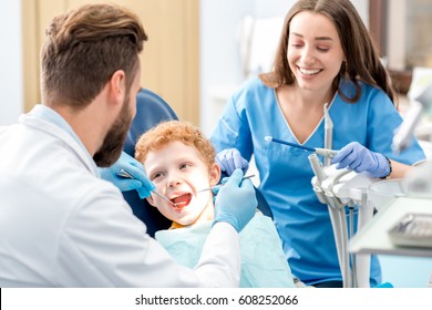 Children's dentist and assistant examinating baby teeth of a young boy sitting on the dental chair at the office
