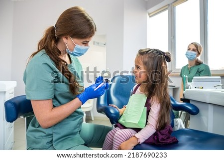 Children's dentist showing on artificial jaw  how to brush teeth. Little female patient sitting on chair and listens to the advice of a dentist