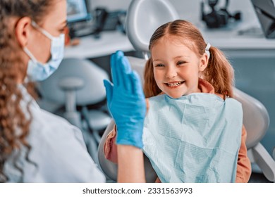Children's dentistry. The child sits in the dental chair and cheerfully gives a high five to the nurse. - Powered by Shutterstock