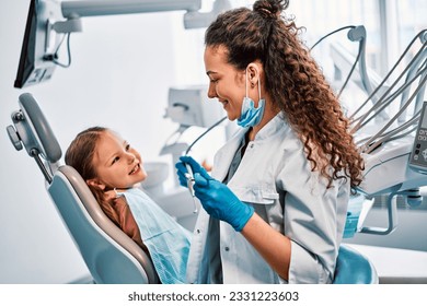 Children's dentistry. A child is sitting in a dental chair and talking to a nurse in dental room. - Powered by Shutterstock