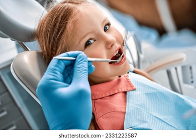 Children's dentistry. Close-up portrait of a girl sitting in a dental chair and having her teeth treated. A doctor in gloves holds instruments. - Powered by Shutterstock