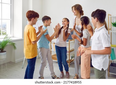 Children's education. Funny schoolchildren and their positive female teacher play fun games in creative lesson. Elementary school students laugh loudly and clap their hands together in classroom. - Powered by Shutterstock