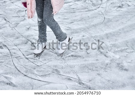 Children's feet in figure skating skates on the beautiful ice of a frozen pond. Snowfall. Copy space.                               