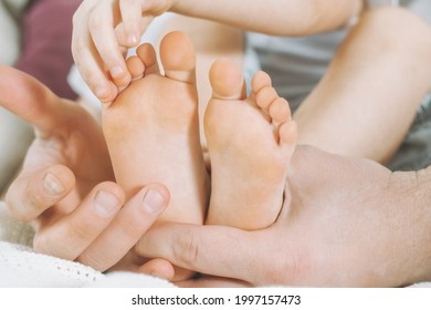 Children's Feet In Hands Of Father. Dad Tickles Feet Of Kid. Baby Counts Toes