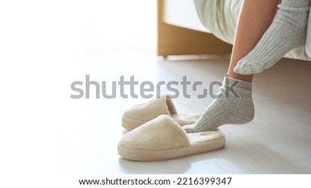 Children's feet in warm socks and slippers. Early in the morning a young girl puts on slippers after sleeping. Comfort and relaxation in the cold season concept