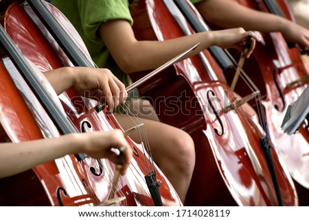 Children's fingers drawing bows across the fingerboards of shiny cellos during outdoor performance
