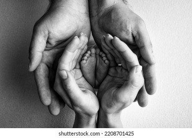 Children's Foot In The Hands Of Mother, Father, Parents. Feet Of A Tiny Newborn Close Up. Little Baby Legs. Mom And Her Child. Happy Family Concept. Black And White Image Of Motherhood Stock Photo.