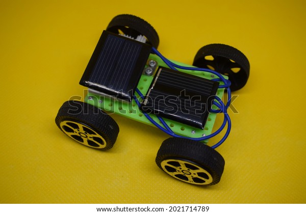 Children\'s green toy with solar panels and\
black wheels isolated on yellow\
background.