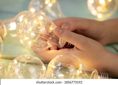 children's hand with a decorative light bulb garland on a light wooden surface close up - Powered by Shutterstock