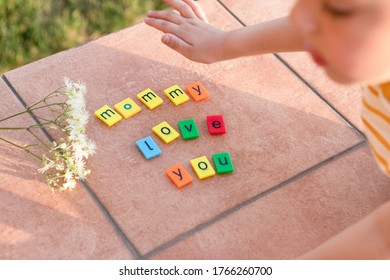 Children's hand puts the words Mommy love you. Multi-colored letters on a brown surface.Cute greeting card. Outside. Concept of love, mothers Day, learning in the game, children's creativity