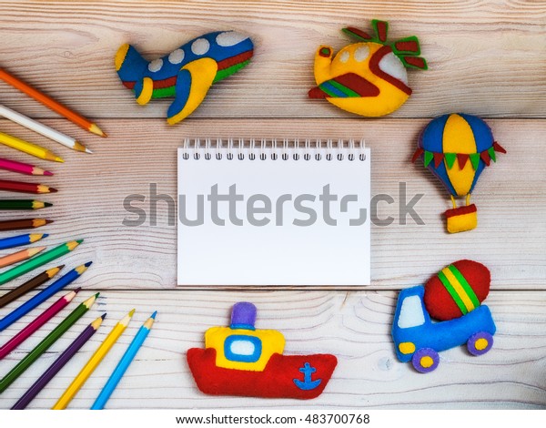 Children\'s handmade toys from felt\
along with colored pencils and notepad on the wooden\
background