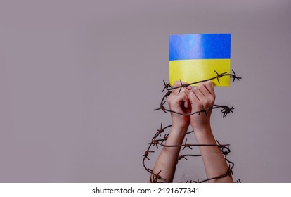 Childrens hands in barbed wire holding flag of Ukraine as symbol of the struggle for freedom and democracy of the Ukrainian people, russia's war and aggression against Ukraine - Powered by Shutterstock