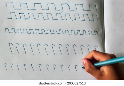Children's hands with a blue pen on the table with a sheet of paper writes squiggles. View from above.