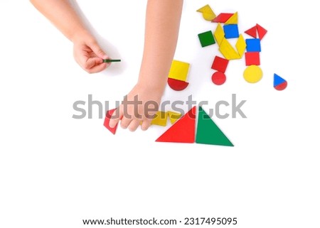 children's hands create pictures from colored wooden geometric shapes, little child, girl 3 years old playing with educational toy, concept children's imagination, unique works art, finished artworks