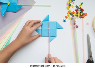 Children's Hands Do Origami On A Table. Nearby Sheets Of Color Paper Lie.