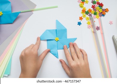 Children's Hands Do Origami On A Table. Nearby Sheets Of Color Paper Lie.