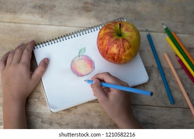 Children's hands draw an apple and colored pencils  Top view