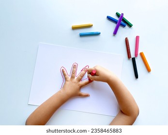 Childrens hands draw their hand with wax crayons on white paper, top view. - Powered by Shutterstock