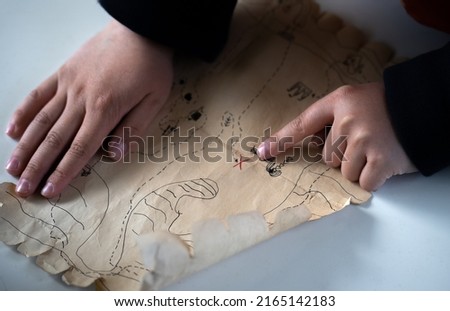 Children's hands hold a treasure map. Search for treasure with a child.Active outdoor games. In search of adventures with children. The map on which the place with the pirate treasure is indicated.