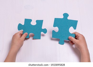 Children's hands hold two puzzle pieces on a light wooden background.