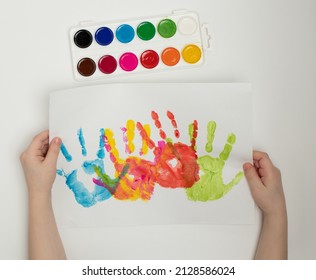 Children's Hands Hold A White Sheet Of Paper With Colored Palm Prints. Finger Painting Or Art Therapy For Children.